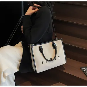 Detalle de un bolso tote grande de lona blanco roto con ribete de cuero negro y logo Paris