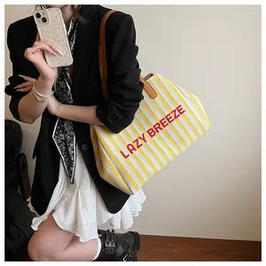 Détail du cabas en toile rayée jaune avec broderie LAZY BREEZE rouge et poignée marron