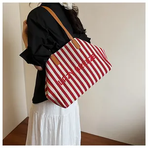 Détail du cabas en toile à rayures rouges avec anses en cuir marron porté par mannequin