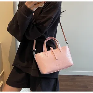 Pink croc-embossed tote bag with top handles and shoulder strap shown on a model