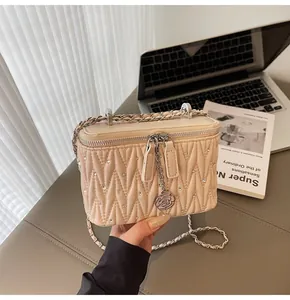 Detail of beige quilted handbag with floral pendant and silver chain strap