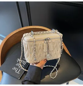 Detail of beige quilted box bag with V-shaped stitching and rose zipper pendants
