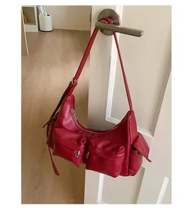 Detail einer weinroten Lederschultertasche mit praktischen Cargotaschen an weißer Tür
