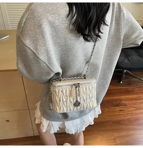 Close-up of beige quilted crossbody bag featuring silver chain and rose metal charm