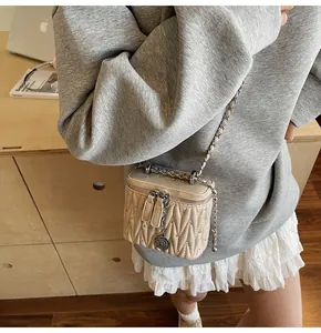 Detail of beige quilted mini crossbody bag featuring rhinestone studs and metal letter pendant