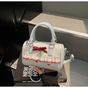 Détail d'un sac Boston chic avec nœud rouge, breloque cœur et bordure en dentelle à la main