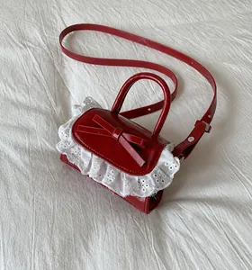 Macro detail of red bow and white lace trim on the glossy leather surface of the small bag