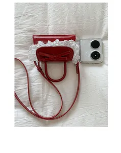 Macro detail of red mini crossbody bag with lace bow and smartphone for size reference