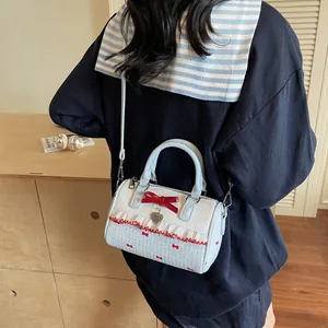 Sac sous le bras matelassé blanc à pois bleus et nœud rouge porté par mannequin
