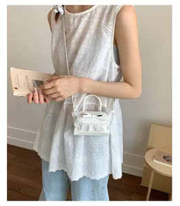 On-body view of a white mini leather crossbody bag with bow and ruffled lace trim
