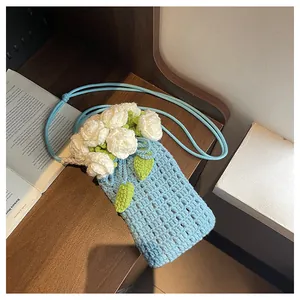 Detalle del bolso de móvil tejido azul claro con flores blancas sobre madera