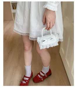 Close-up of a white mini handbag with lace trim and bow, held by a model in a dress