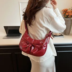 Fashionable red pleated underarm bag with bow decoration shown on a shoulder