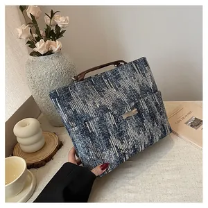 Close-up of blue-grey tweed tote bag with dark brown leather handles and silver accents