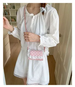 Pink polka dot mini shoulder bag with lace edges worn over a white dress
