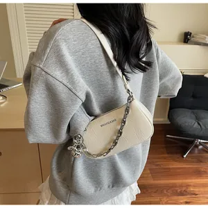Close-up of a cream textured leather shoulder bag featuring a silver chain and rabbit charm