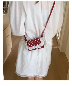 Detailed view of mini red polka dot crossbody bag with white lace trim on white dress
