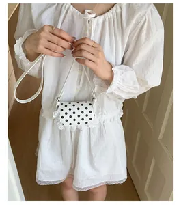Detailed view of a white lace polka dot mini crossbody bag worn by a model
