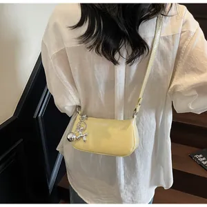 Detail of light yellow leather shoulder bag with silver balloon dog charm and embossed logo