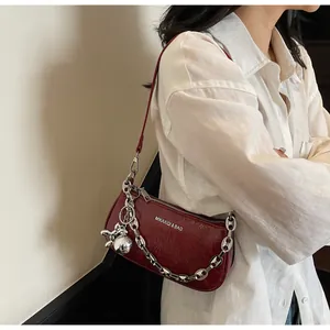 Detail of burgundy patent leather crescent bag with silver chain and artistic charm