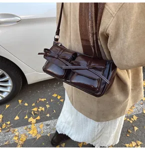 Detail der dunkelbraunen Lackleder-Umhängetasche mit Schleifentaschen in Straßenszene
