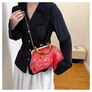 Détail du sac coquille brodé rouge avec poignée en bambou et accessoire de pompon