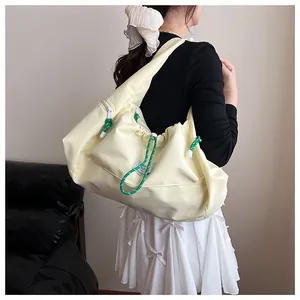 Dettaglio della borsa a spalla in nylon crema con coulisse verdi e chiusura a sacco