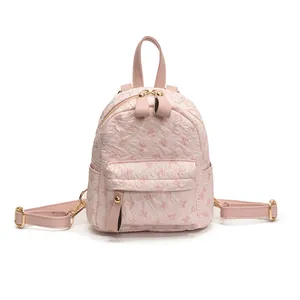 Pink mini backpack with embossed bow textures and gold zippers on white background
