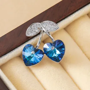 Broche de cereza con corazón de circón azul en plata sobre un joyero de terciopelo