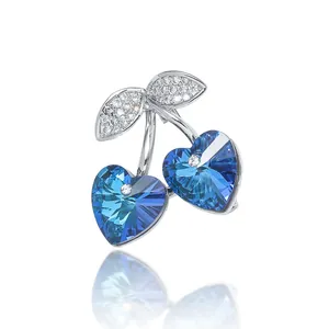 Broche de cereza corazón azul con circón y hojas plateadas sobre un fondo gris liso