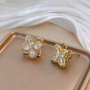 Close-up of golden four-leaf flower earrings with zircon petals and micro-pave crystals