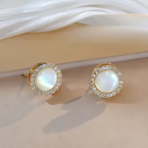 Macro detail of gold stud earrings with mother of pearl inlay and sparkling zircon halo