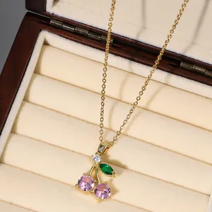 Detailed view of cherry pendant necklace with pink stones on a beige velvet jewelry box