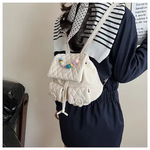 Quilted cream backpack with colorful beaded handle and drawstring closure shown on model