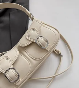 Detalle de bolso de hombro blanco crema con dos bolsillos delanteros y hebillas de metal