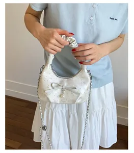 White pleated crescent bag with pearl charm and bow detail shown on a model's shoulder