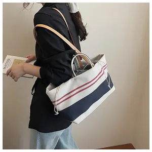 Detail of canvas tote bag featuring contrast leather handles and striped drawstring liner