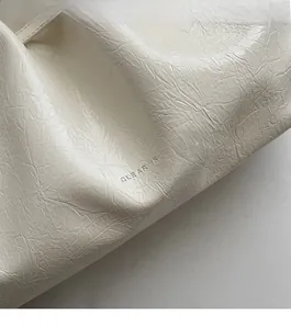 Detail of pearl white pleated leather tote showing high-quality debossed brand logo