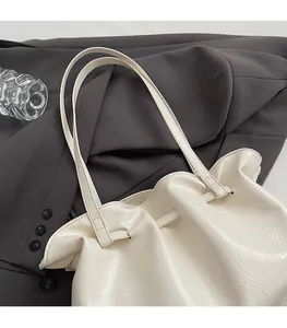 Close-up of cream textured leather tote bag with thin double straps on a gray blazer