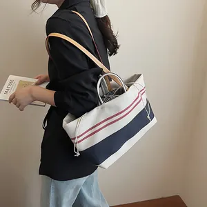 Large striped canvas tote bag with leather straps and drawstring closure shown on shoulder