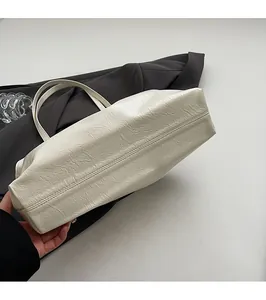 Detail view of the flat bottom and pleated oil wax leather texture on the cream tote bag