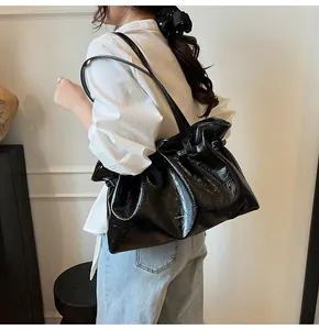 Detail of black glossy crinkled leather tote bag with long straps and brand lettering