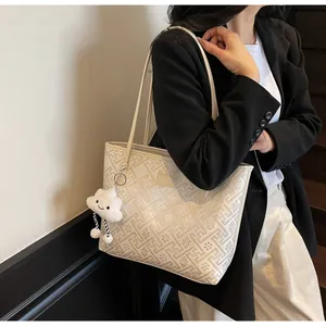Close-up of beige printed tote bag with leather strap and cloud charm on a model