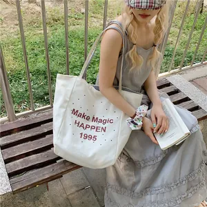 Large off-white canvas tote bag with red lettering and blue striped straps in outdoor setting
