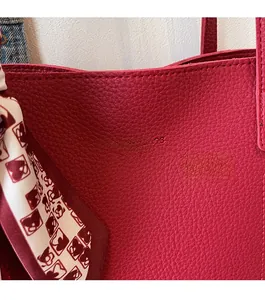 Macro detail of dark red pebbled leather bag with silk scarf and embossed logo