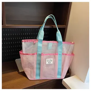 Detail of pink mesh tote bag with blue straps and side pocket on wooden shelf