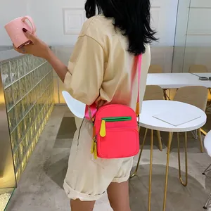 Neon pink oxford cloth crossbody bag with contrast green zippers in a stylish cafe setting