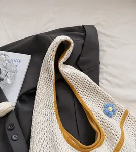 Nahaufnahme der beigen Häkeltasche mit gelbem Rand und blauer Häkelblume am Riemen