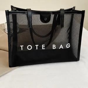 Detalle del bolso tote de malla negra con estampado TOTE BAG y acabados de cuero liso