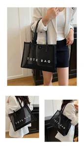 Detalle del bolso tote de malla negra con texto blanco y correas de hombro de cuero
